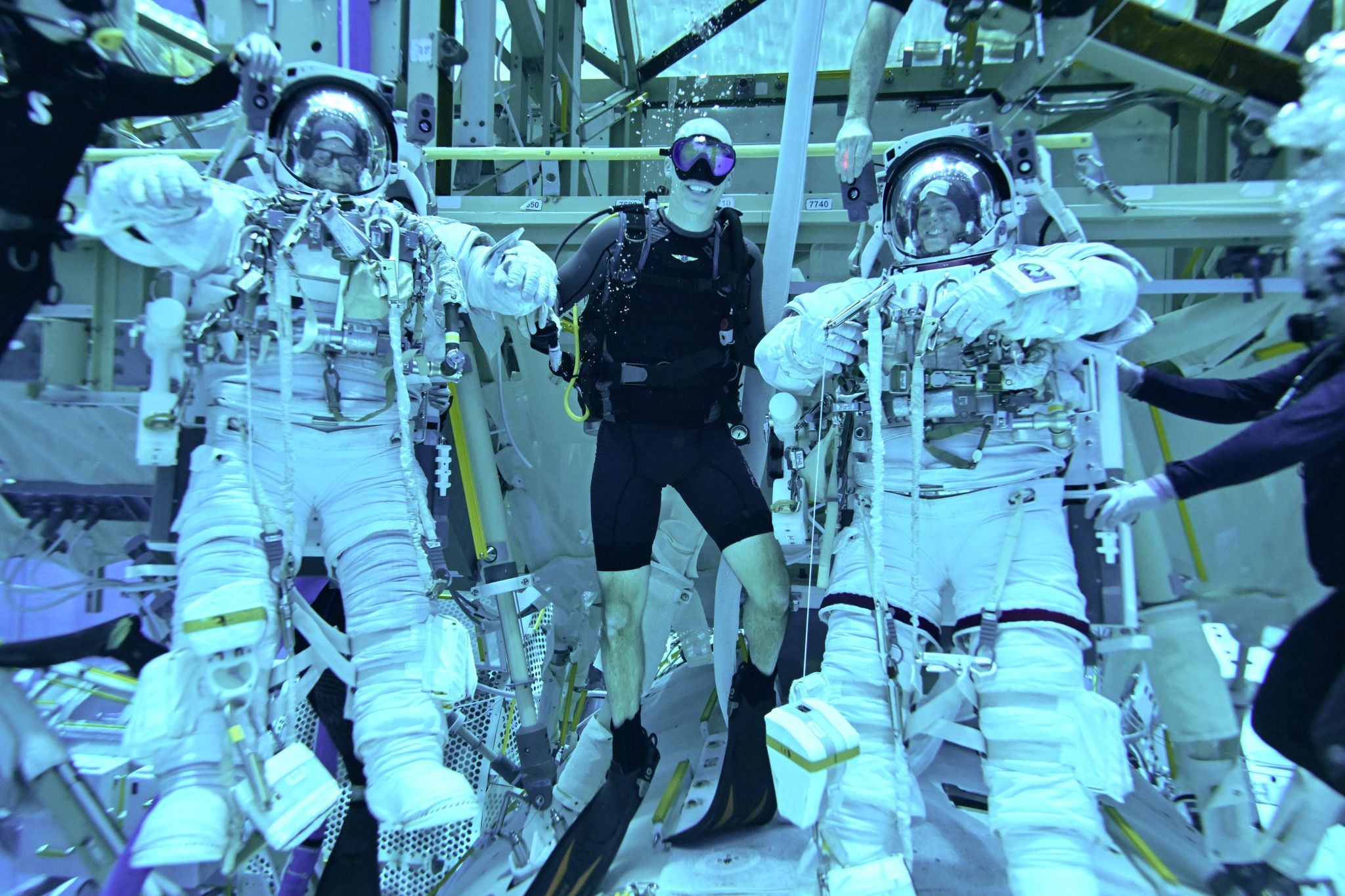 Underwater image in training facility with three people; one in scuba gear and two in space suits.