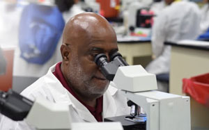 A man in a lab coat looks into a microscope in a lab setting