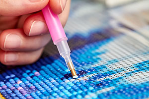 A close-up of someone's hand using an applicator pen to apply dots to a canvas