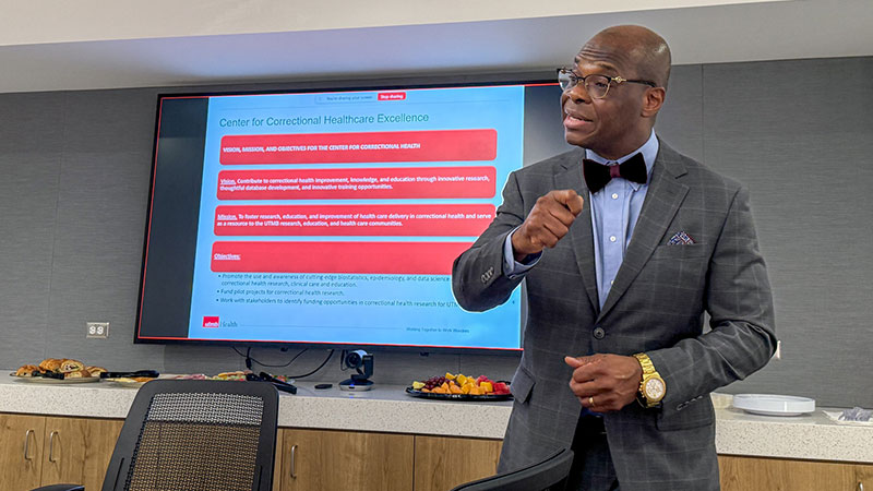 Dr. Olugbenga Ojo holds a microphone in front of a screen, presenting on the Center for Correctional Health
