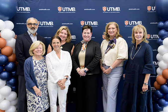 A group of leaders from UTMB and the Sealy & Smith Foundation pose in front of a dark blue UTMB backdrop with balloons on both sides.