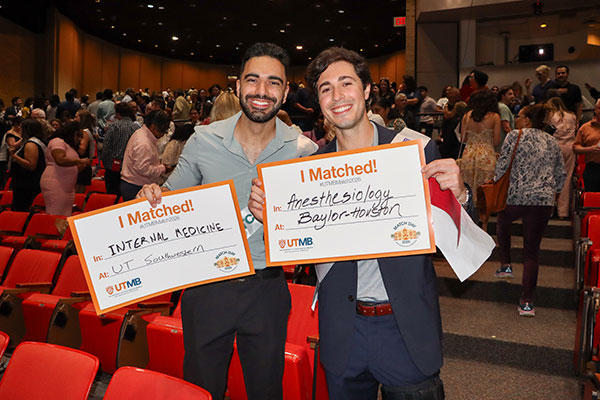 Two men hold their Match Day posters during UTMB's ceremony in Levin Hall. One shows that he matched in Internal Medicine at UT Southwestern; the other matched in Anesthesiology at Baylor Houston.
