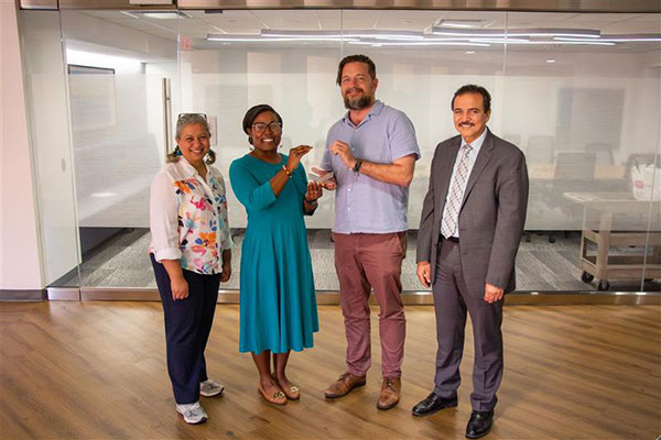 Dr. Hanaa Sallam, Dr. Mandy Hill, Dr. Michael Goodman and Dr. Hani Serag pose together. Dr. Hill is handing Dr. Goodman a glass award statue.