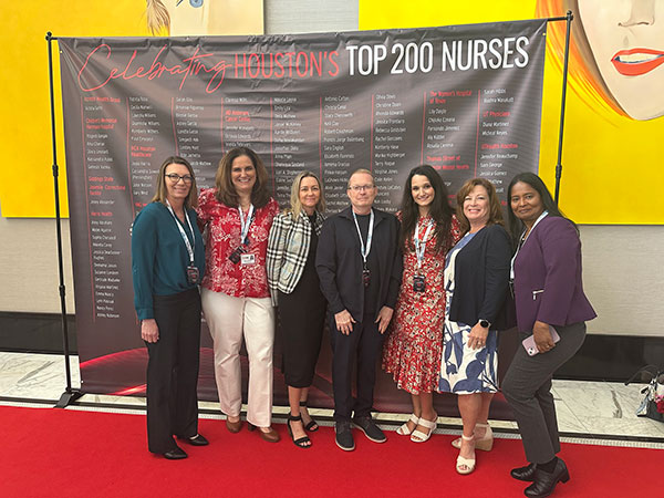 UTMB nurses and guests pose on a red carpet in front of the Salute to Nurses list of honorees.