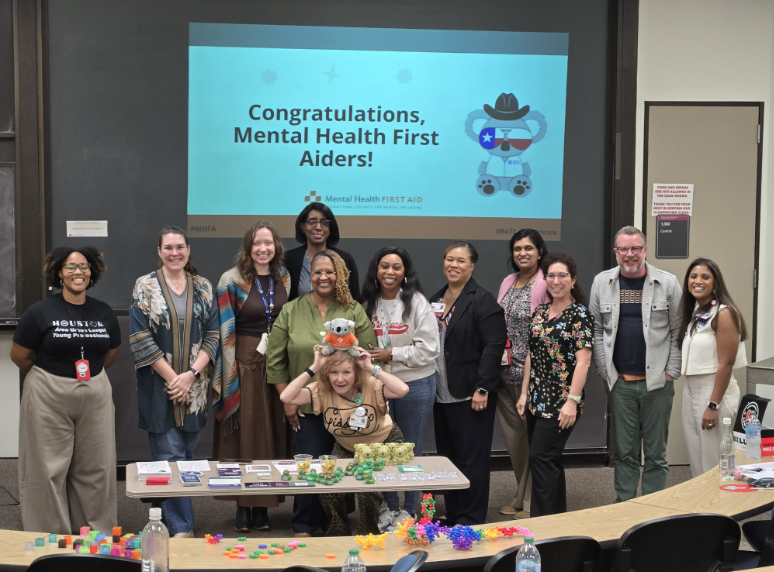 School of Nursing faculty and staff members pose with an assortment of colorful blocks and toys in front of a screen that says "Congratulations, Mental Health First Aiders!"