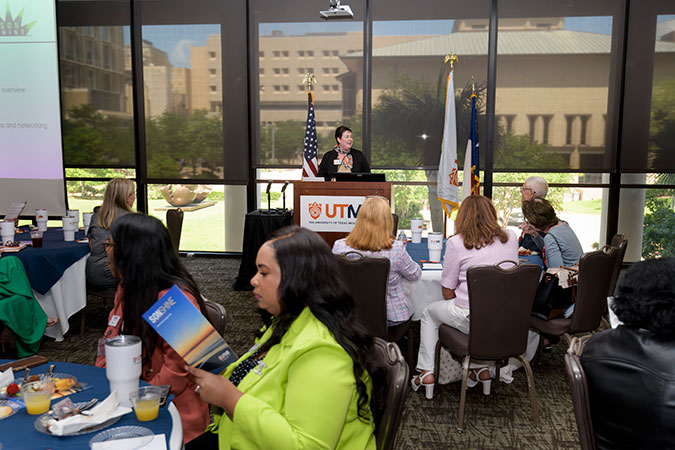 Interim Dean Dr. Kristen Starnes-Ott stands at the podium before an audience of guests at tables.