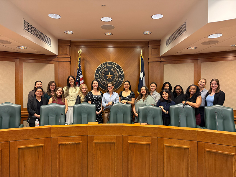 A group of 17 nursing students stand posed inside the Texas State Capitol, with the state seal in the background.