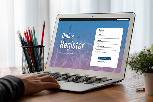 A man's hand rests on the keyboard of a laptop that displays a registration screen