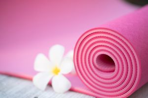 A pink yoga mat is partially rolled up, with a white flower at the edge