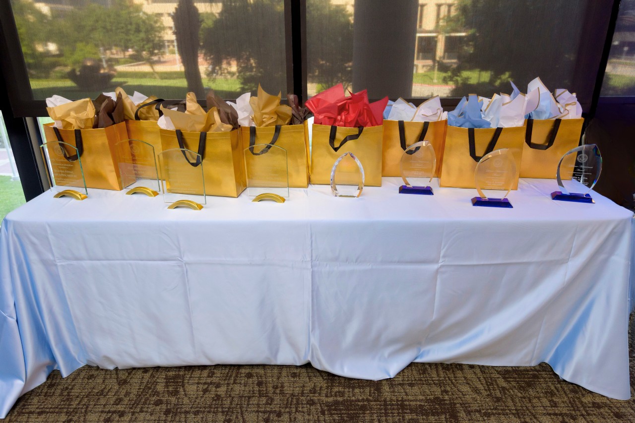 table with light blue table cover, eight gold gift bags with different colored tissue paper and eight crystal plaques in front of the bags.