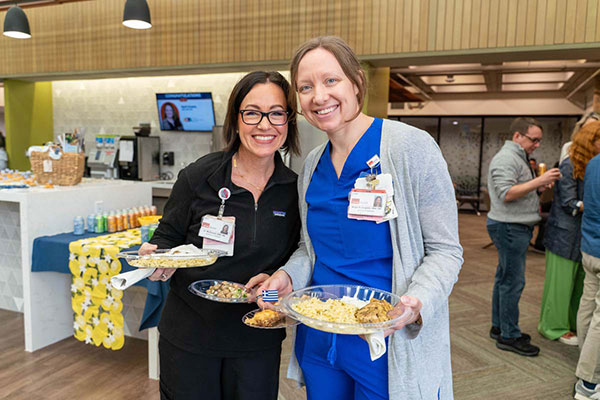Two UTMB School of Nursing faculty members, Dr. Jo McDonald and Dr. Morgan Cangelosi, pose together at the faculty luncheon. They are holding plates of food inspired by Ikaria, Greece.