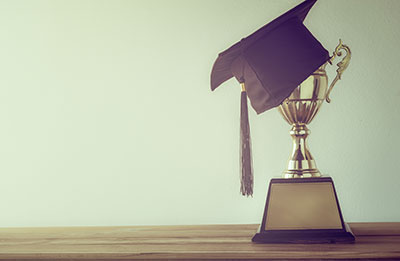A black graduation cap sits atop a gold cup-style trophy