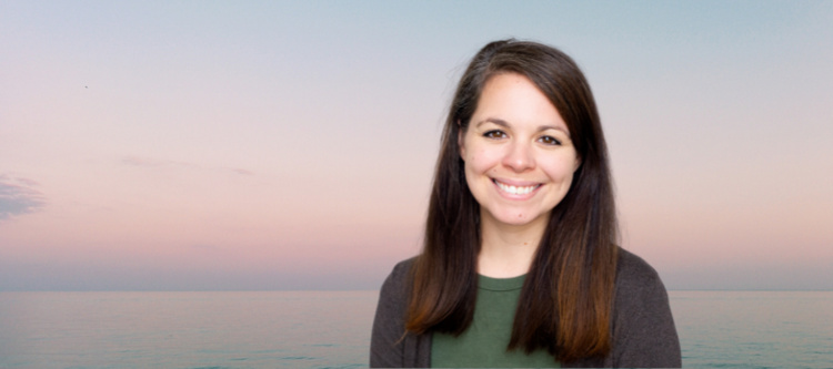 A woman with brown hair in front of a sunset beach background is smiling
