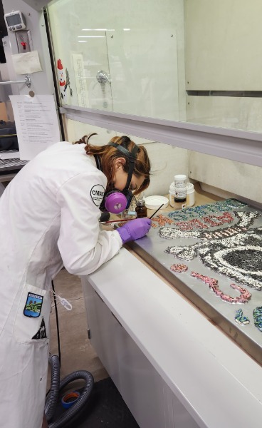 A conservator in a white coat is leaning over a table and working with specimens