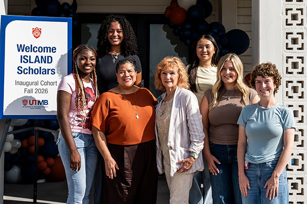 The ISLAND Promise Scholars, Dr. Deb Klesel and Dr. Martina Gallagher pose in front of the Botanical building next to a welcome sign.