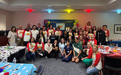 SHP Clinical Laboratory Sciences faculty and staff gather in a room decorated with colorful table cloths and balloons.