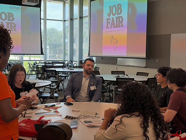 MLS students and lab professionals have a conversation at a round table; a screen behind them shows the Job Fair logo.