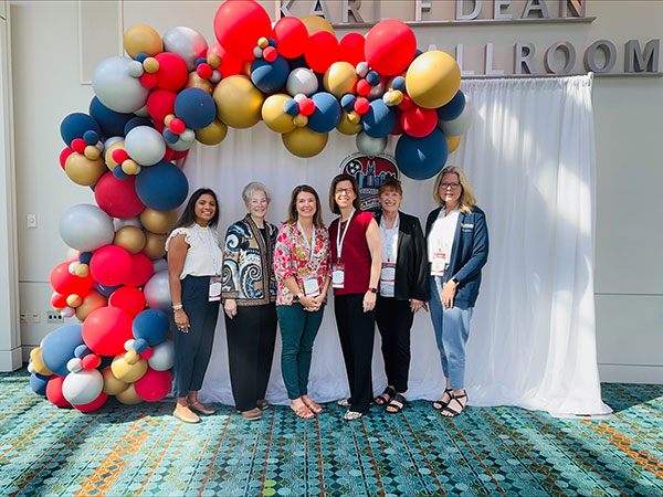 UTMB SON faculty pose in front of a convention backdrop and balloons