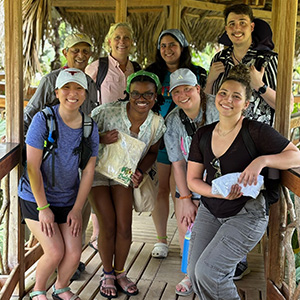 Nursing - Belize 2 A group of nursing students and Prof. Christen Sadler pose standing under a thatched roof