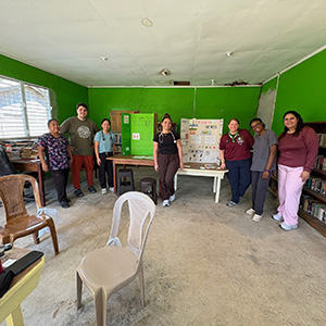 Nursing - Belize 5 A group of nursing students and Hillside Health staff stand all the way across a room with green walls, with scientific posters on display between them.