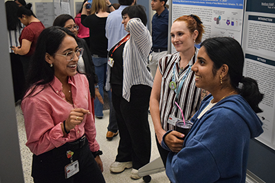 poster session 4 Three women stand between mounted posters at the poster session, smiling and talking.