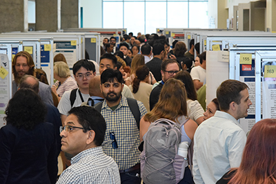 poster session Poster session attendees fill the presentation area, where posters are displayed on both sides of an aisle.