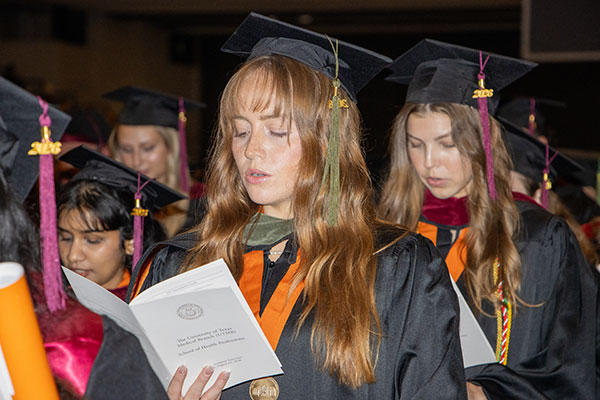 Graduates recite their oath at SHP commencement; in the forefront is a woman with long red hair reading from her program booklet