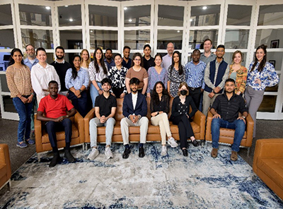 A large group of summer camp participants posed for a group photo. Some are seated on brown chairs and others are standing behind them.