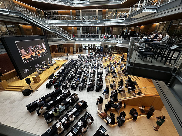 An aerial shot of the Texas Brain Economy Summit, showing attendees around the room at tables and seated on a bleacher staircase