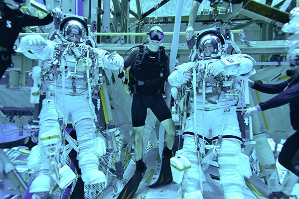 Two individuals in space suits, with others in wet suits, pose in a training environment