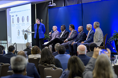 Panelists sit in a row on stage in front of a large crowd