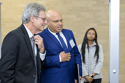 Two men in suits look at a displayed posted; a woman in the background observes.