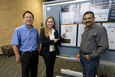 Three UTMB faculty members stand in front of a displayed poster