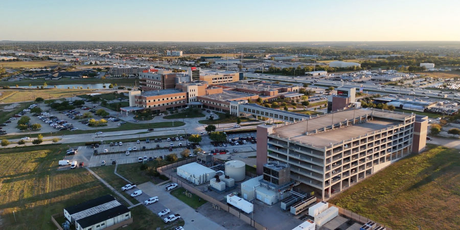 Aerial view of a large medical campus surrounded by parking lots, roads, and nearby commercial buildings.