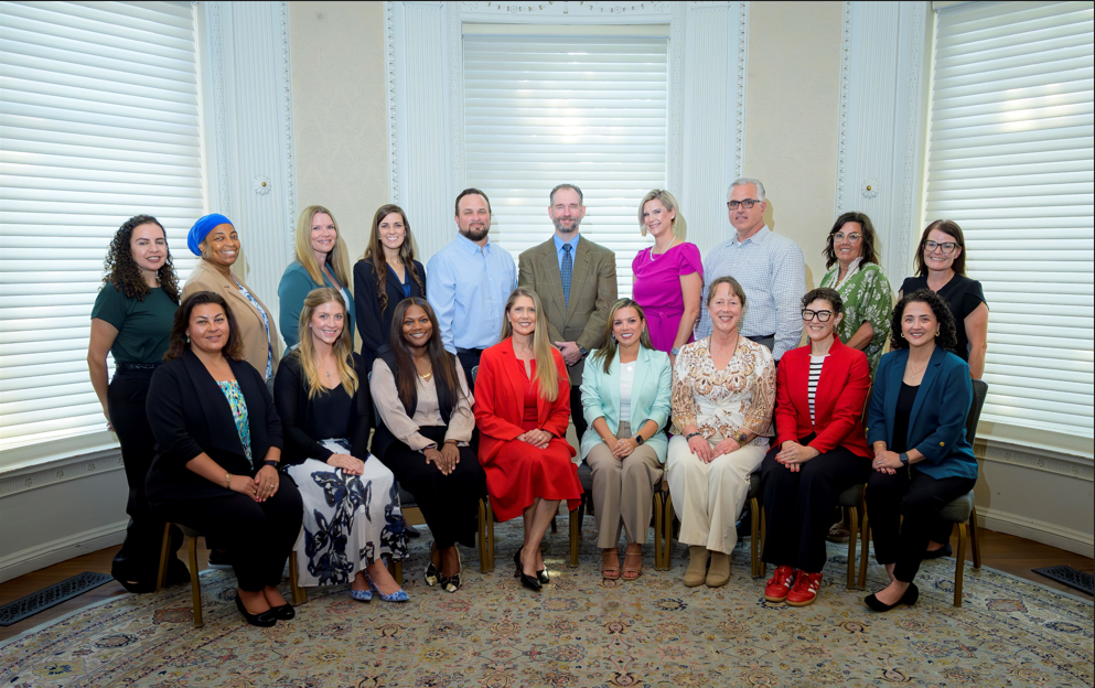 Group portrait of UTMB Employee Advisory Council members seated and standing in two rows inside a formal room with tall windows and neutral décor.