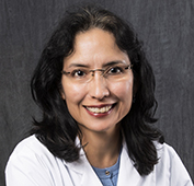 Picture of a woman smiling wearing glasses with shoulder length dark hair with a white lab coat