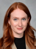 Image of a lady with auburn hair wearing a tan and black shirt