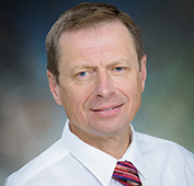 Picture of a man smiling wearing a white shirt and multiple colored tie