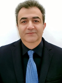 Image of a man in front of a white background wearing a black suit and blue tie