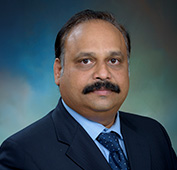 Picture of a man with a dark suit, blue shirt and a mustache