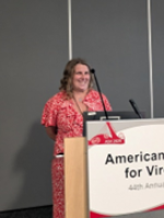 Picture of a woman smiling wearing a red dress standing behind a podium