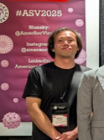 Picture of a man smiling standing in front of a ASV2025 poster