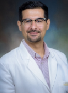 Image of a man in a white lab coat, pink shirt wearing glasses