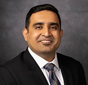 Picture of a man smiling wearing a black suit and multi-colored tie