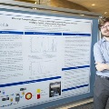 UTMB pathology resident Eric presenting research at a medical conference, standing near a poster display and engaging with academic peers.