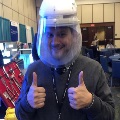 UTMB pathology resident wearing a protective face shield and giving a thumbs-up while standing at a conference exhibit booth with medical tools displayed on a table.