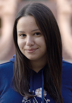 Picture of a woman smiling with long dark hair, blue sweatshirt standing outside