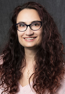 Picture of a woman smiling wearing glasses with long, brown curly hair