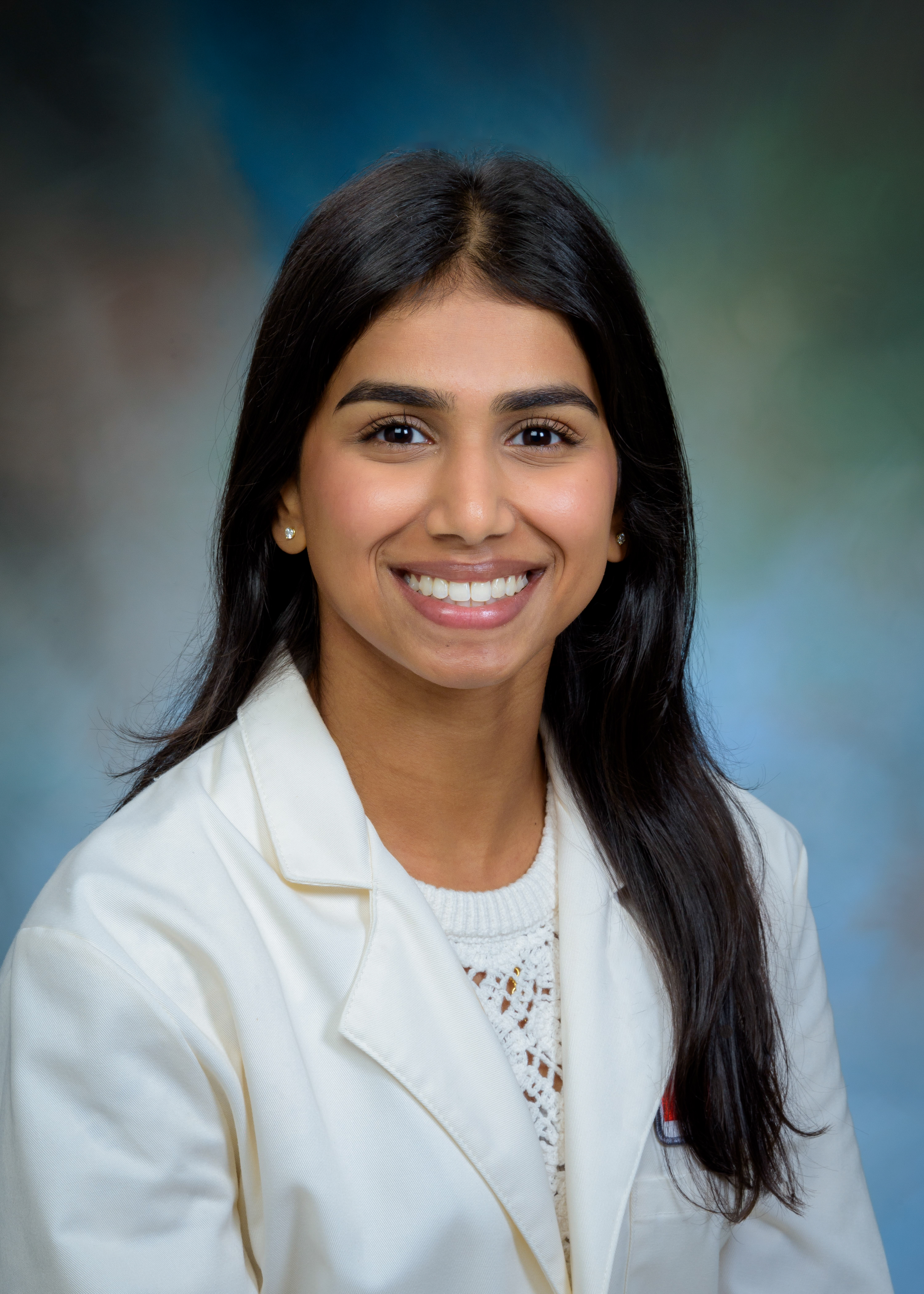 Studio portrait of a pharmacy preceptor wearing a white coat over a light top, photographed against a softly blended neutral background.