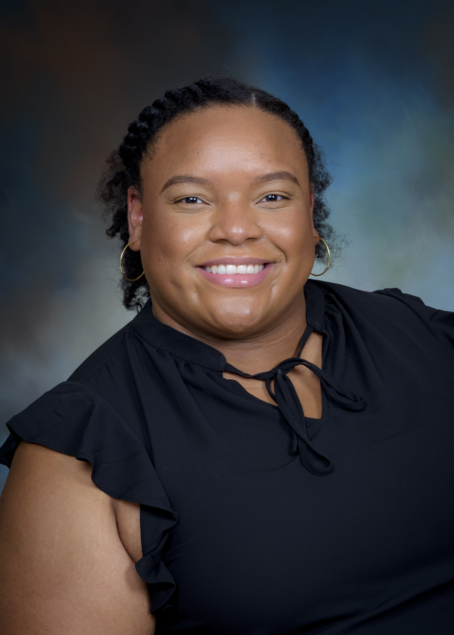Studio portrait of a pharmacy preceptor wearing a black blouse, photographed against a softly blended neutral background.